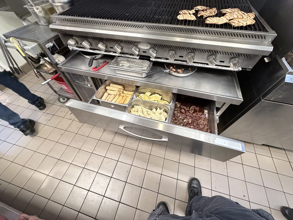 Refrigerated chef base drawers open under a commercial char grill