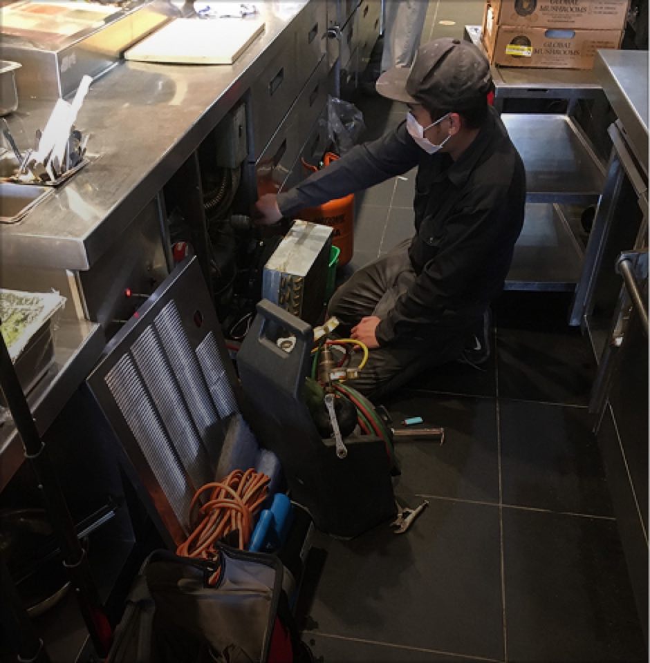 Cool Aid technician repairing refrigeration equipment behind a counter