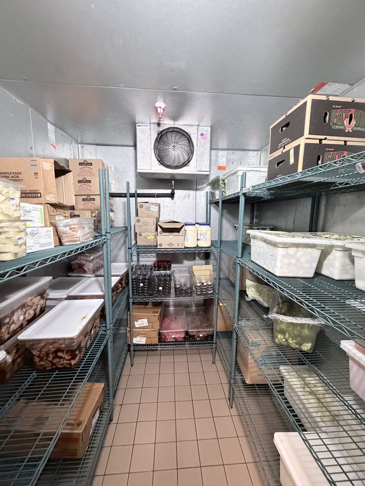 Inside a stocked restaurant walk-in cooler with the evaporator on the back wall